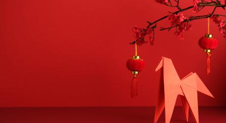 An origami paper horse, red lantern, and plum blossom branch against a bright red background. 