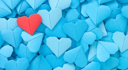 Blue origami hearts with one single red heart on top of pile.