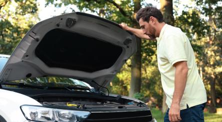 Man looking under hood of car outdoors.