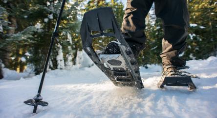 Close up shot of snowshoe clad feet traipsing over the snow with a forest in the background.