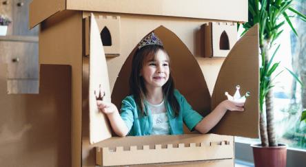 Child dressed as princess playing in a cardboard fort.