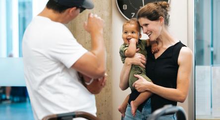 Mingling after Storytime at Terry Fox Library: a man waves to a a baby being held in his mother's arms.
