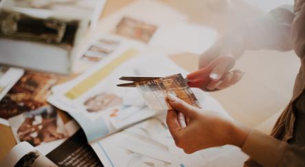 Pair of hands with scissors cuts out magazine pictures to make collage.