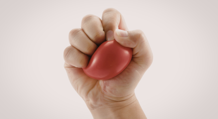 Pale hand squishing a red stress ball on a beige background.