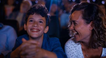 Mid-shot front view of happy young boy and his mother having a good time while sitting inside movie theater.