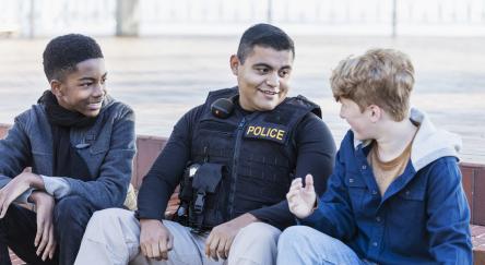 A police officer connects with community youth by chatting with two young teen males.