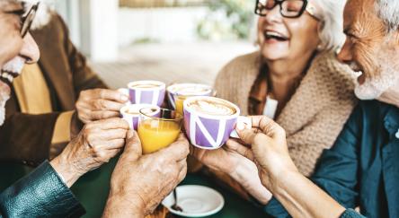 Senior people group toasting with lattes at coffee bar.