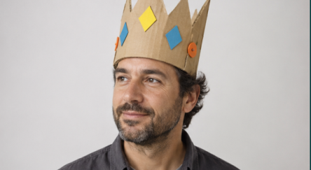 A smiling man wears a cardboard crown.