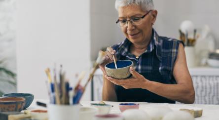 Senior woman decorating bowl made of clay on ceramics workshop.