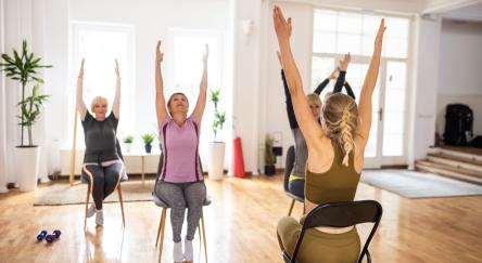 Female yoga instructor having yoga class with senior people on chairs in yoga studio.