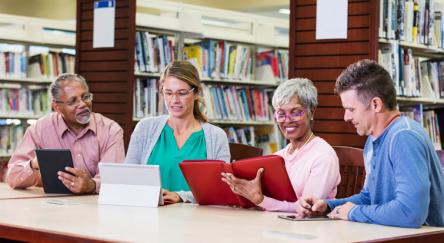 Group of adults in library looking at tablets at a table