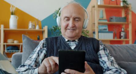 A older man sitting in a living room in headphones using a smart phone