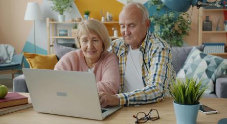 Senior couple using a laptop computer on a desk in a bright day lit living room.