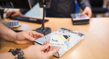 Hands hold an FVRL library card as other hands check out items.