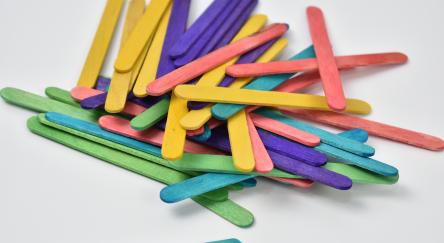 Multi-coloured wooden popsicle sticks sit in a big pile on table.