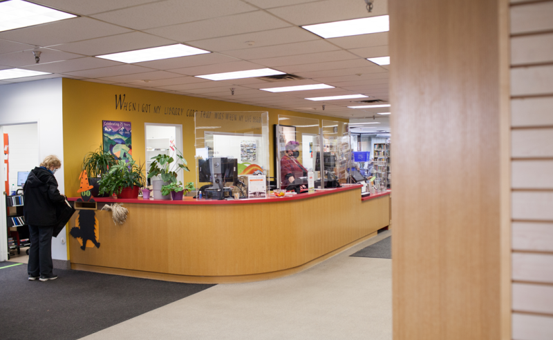 Inside Tsawwassen Library, a woman stands in front of the information desk, engaging with the library's resources.