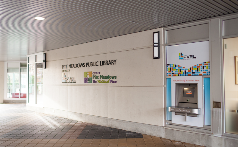 Pitt Meadows Public Library's white facade stands out, featuring large windows and an exterior book drop.