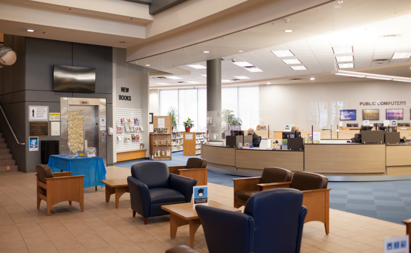 Interior of Maple Ridge Public Library featuring a spacious desk and chairs surrounded by shelves of books.