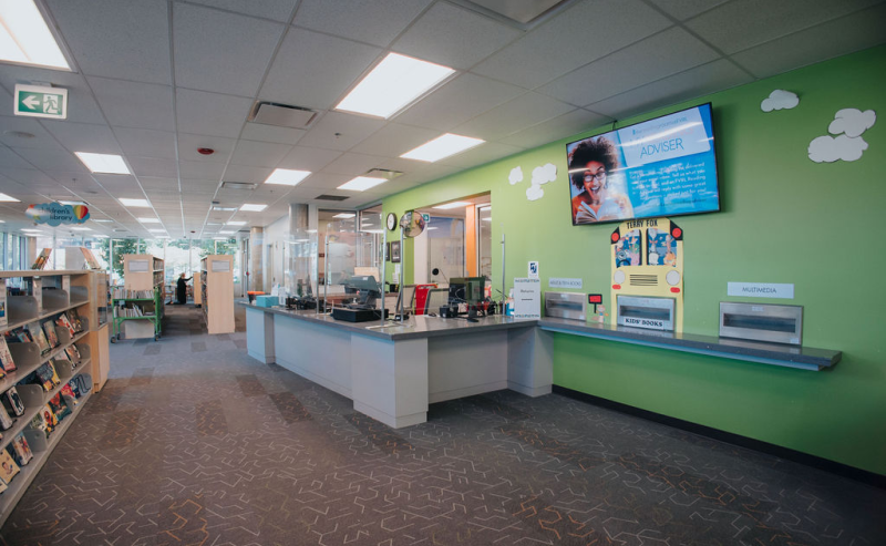 Inside Terry Fox Library, a spacious area showcases a large wall screen amidst rows of books and study spaces.