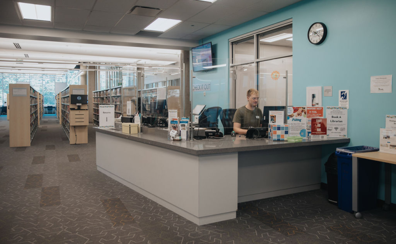 Information desk and staff member inside the Terry Fox Library, surrounded by books and a welcoming atmosphere.