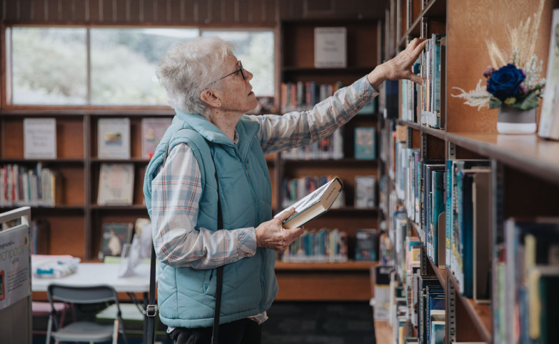 An elderly woman examines books in the warm setting of Mount Lehman Library.