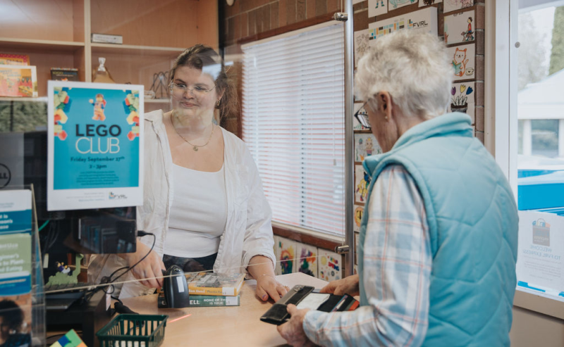 Inside Mount Lehman Library, an elderly woman checks out their books at the information desk.