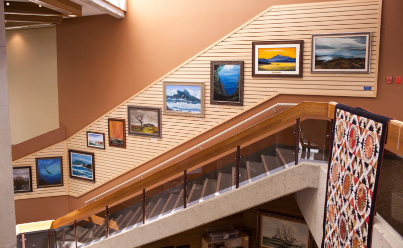 Interior view of White Rock Library's stairway to the second floor, featuring artwork by local artists on the wall..