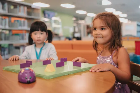 two young kids in the library interacting with robot mouse.