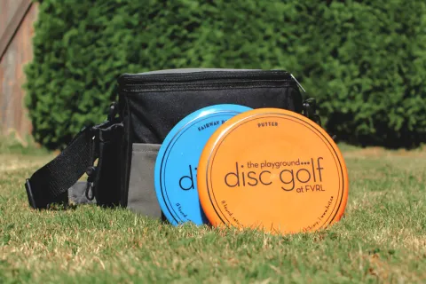 Golf discs alongside a bag of golf discs placed on lush green grass, perfect for outdoor fun.