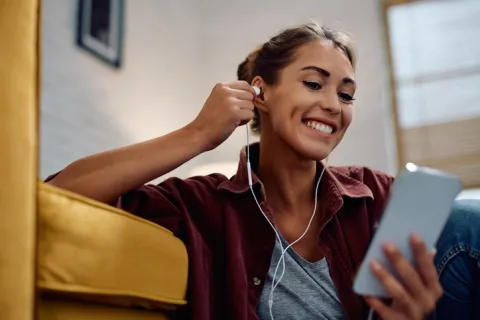 A young woman listens to an audiobook on a mobile devise. She places a white earbud in her hear.