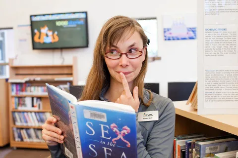 An FVRL staff reads a book titled "Sex in the Sea." She has a mischievous expression on her face.