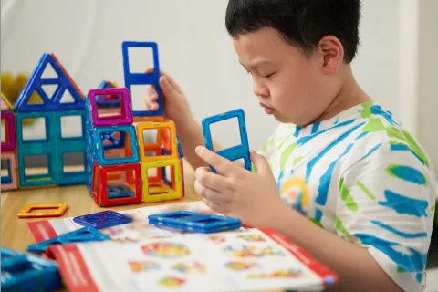 Young boy builds using magnetic Magformer pieces.