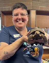 FVRL Reading Adviser Carissa smiles while holding a turtle.