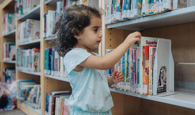 A young girl selects a picture book off the shelf at Abbotsford Community Library.