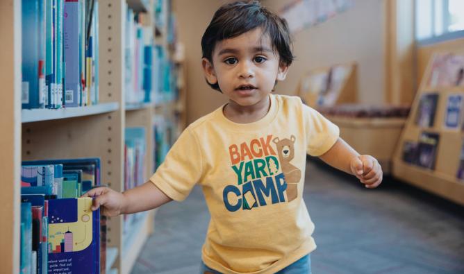 Toddler in yellow shirt running between library bookshelves.