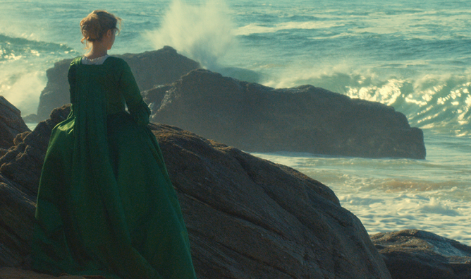 A woman wearing a green dress poses on a rock, showcasing her elegance against a natural backdrop.