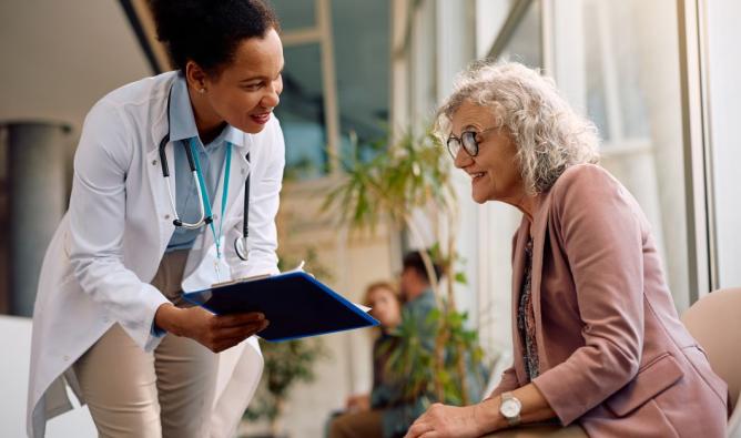 Smiling senior woman and her doctor going through paperwork in hallway at medical clinic.