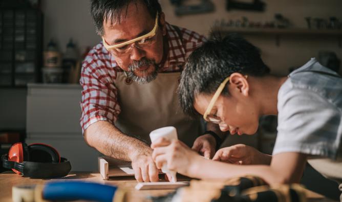 A senior carpenter teaches his grandson woodwork.