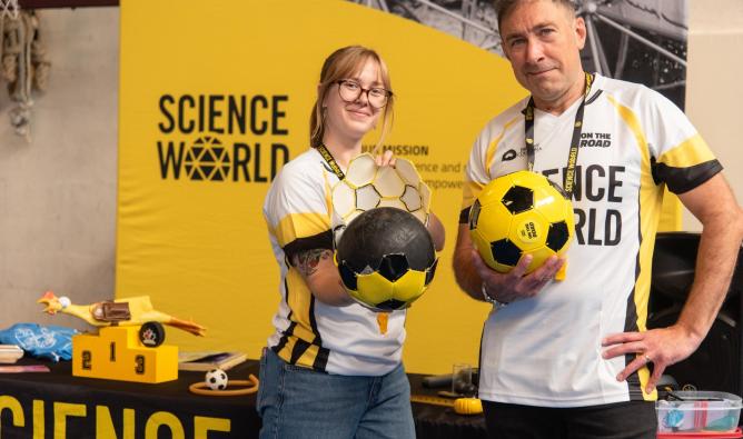 A man and woman holding soccer balls. They are standing in front of a Science World banner.