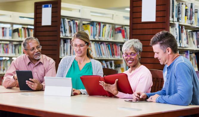 Group of adults in library looking at tablets at a table