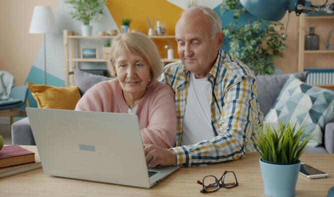 Senior couple using a laptop computer on a desk in a bright day lit living room.