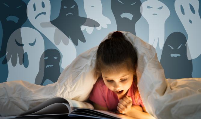 A girl reads a spooky picture book under the covers of her bed. Ghostly images float above her.