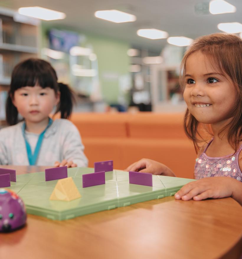 two young kids in the library interacting with robot mouse.