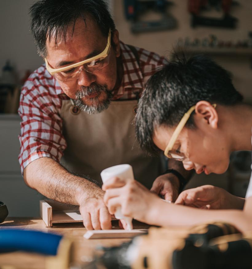 A senior carpenter teaches his grandson woodwork.