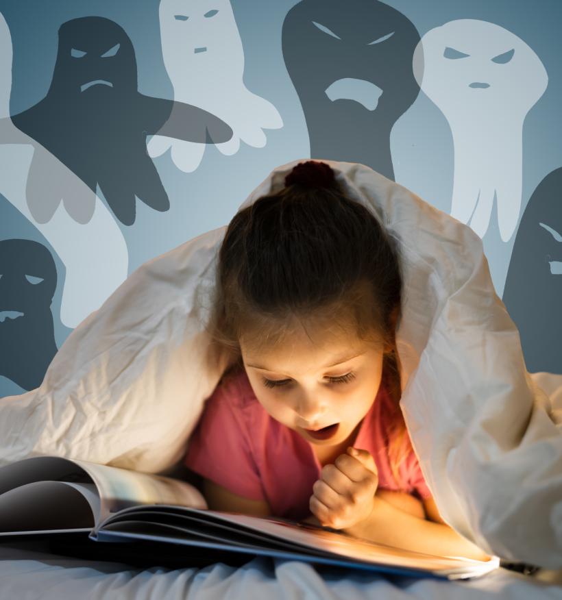 A girl reads a spooky picture book under the covers of her bed. Ghostly images float above her.